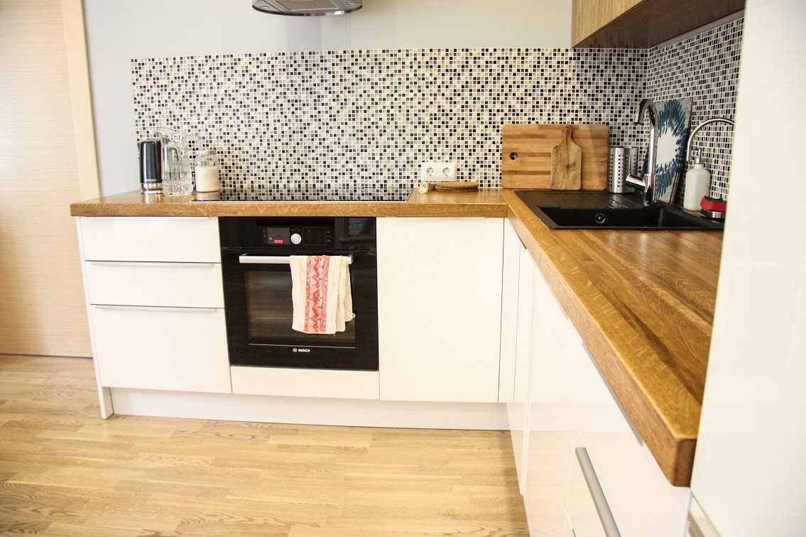 Белая кухня с деревянной столешницей и фартуком в интерьере, глянец с декором
 - 23 фото